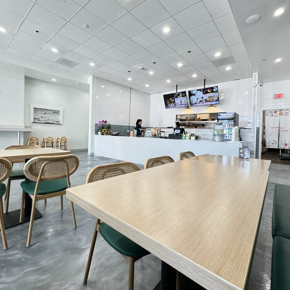 Bright, modern interior of Jack's Bao restaurant with light wood tables, green chairs, and a service counter.