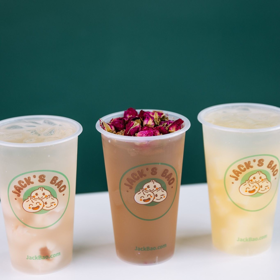 Three Jack's Bao drinks: lychee, rose-topped milk tea, and pineapple, against a green background.