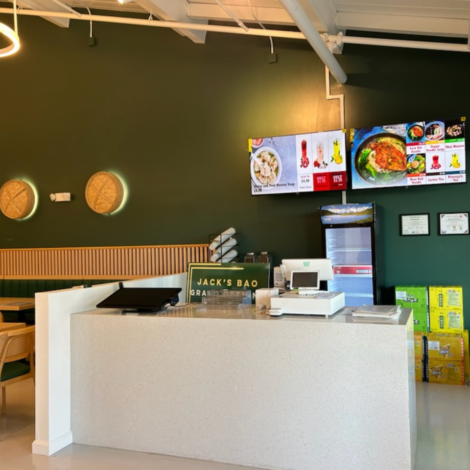 The interior of Jack's Bao features a counter, menu screens, and green walls with decorative bamboo steamers.